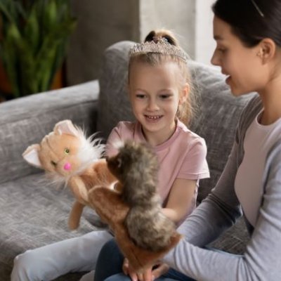 a child and a woman sit on a grey couch holding two animal puppets